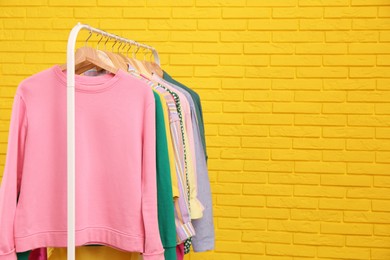 Rack with stylish clothes near yellow brick wall, space for text