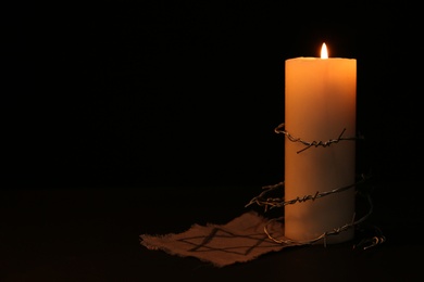 Photo of Fabric with star of David, barbed wire and burning candle on black background, space for text. Holocaust memory day