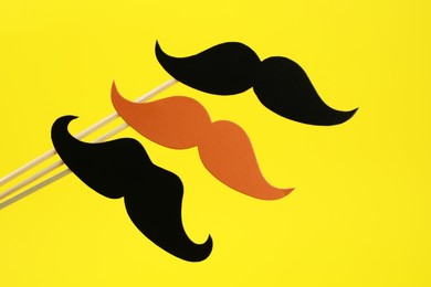 Photo of Fake paper mustaches on sticks against yellow background