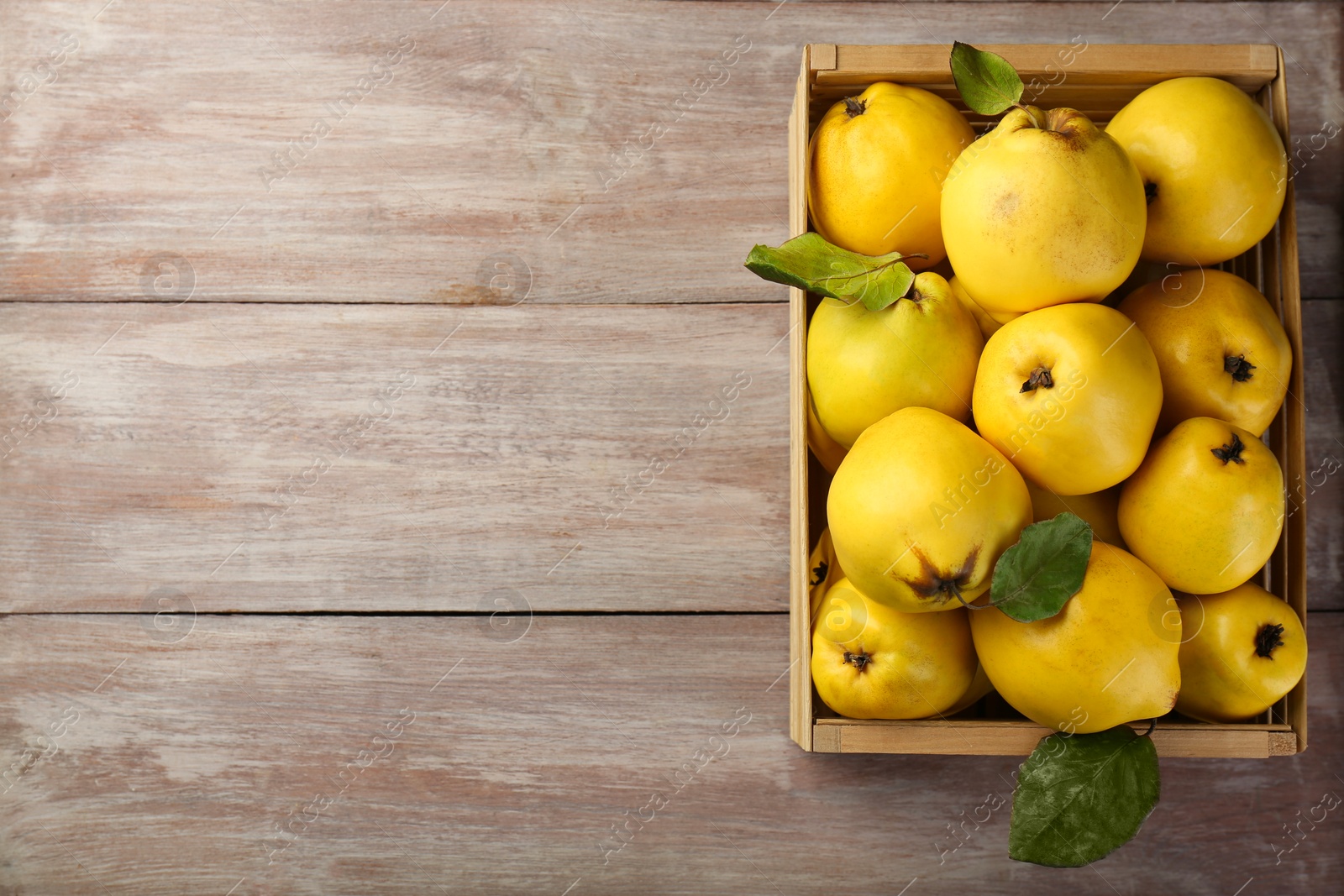 Photo of Tasty ripe quince fruits in crate on wooden table, top view. Space for text