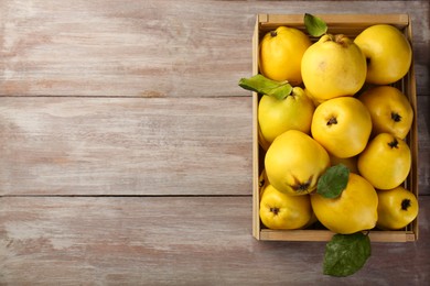 Tasty ripe quince fruits in crate on wooden table, top view. Space for text