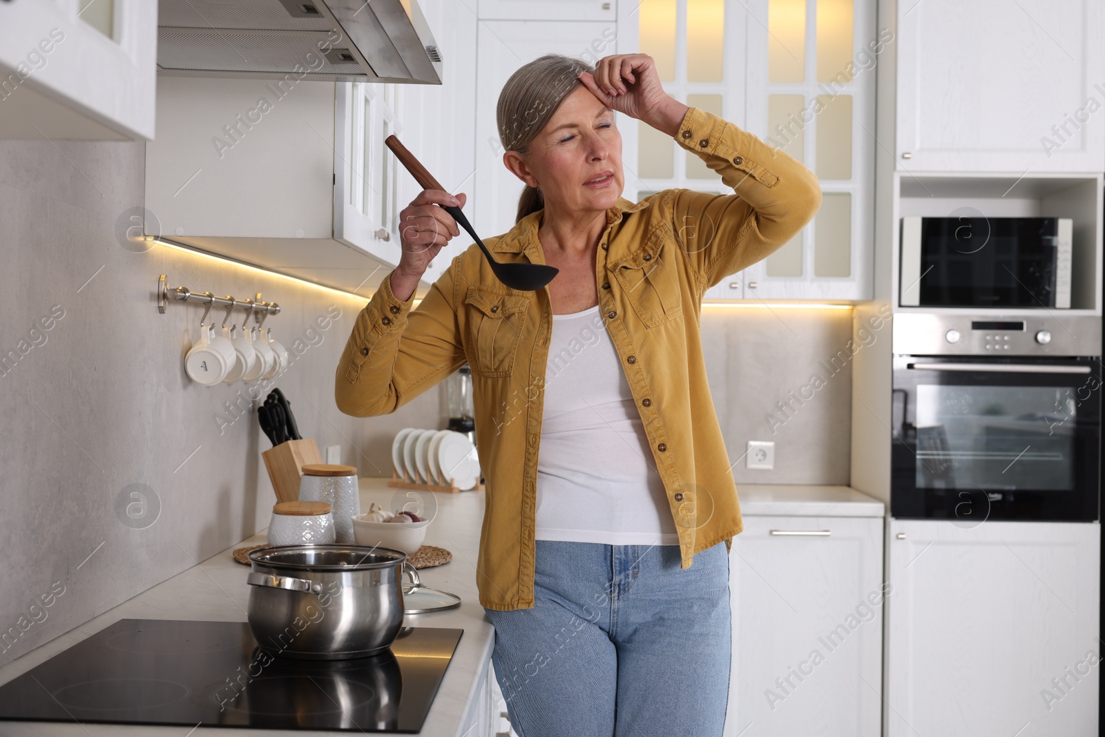 Photo of Menopause. Woman suffering from headache while cooking in kitchen