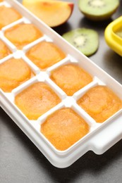 Photo of Nectarine puree in ice cube tray and ingredients on grey table, closeup
