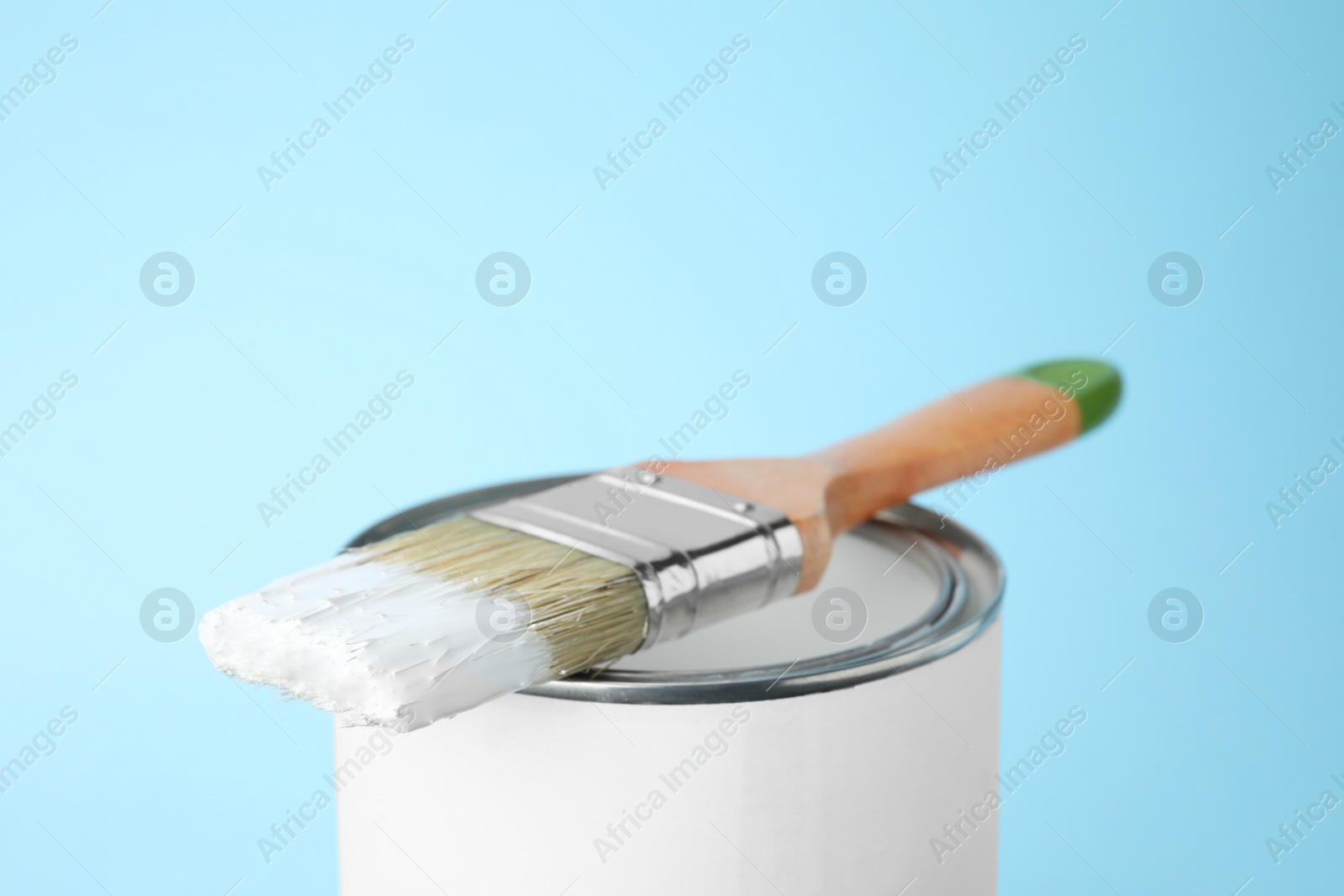Photo of Can of white paint with brush on blue background