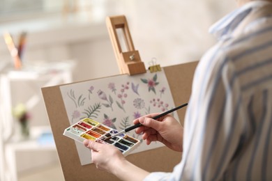 Photo of Woman painting flowers with watercolors in workshop, closeup