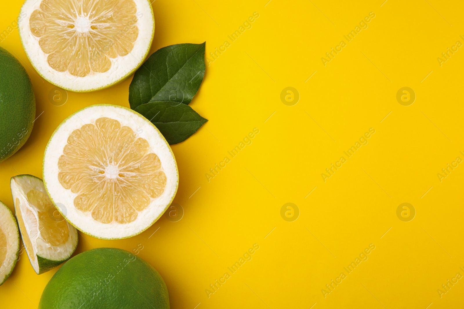 Photo of Whole and cut sweetie fruits with green leaves on yellow background, flat lay. Space for text