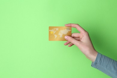 Woman holding credit card on light green background, closeup