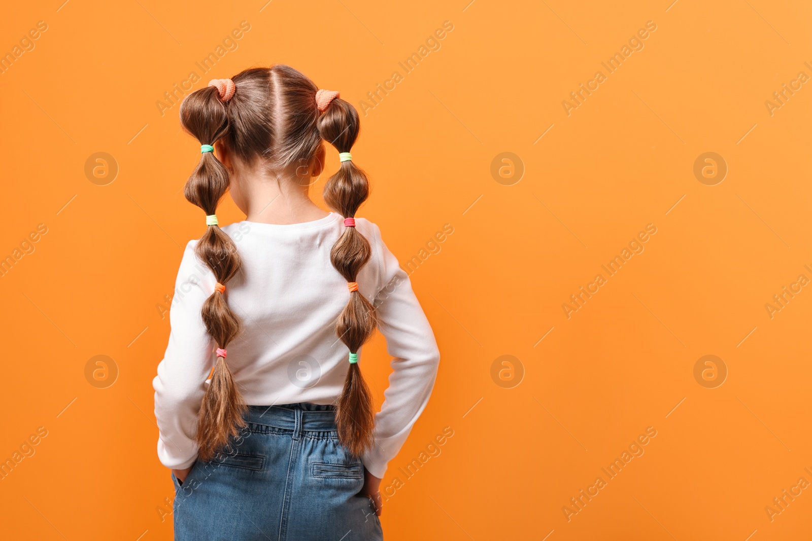 Photo of Little girl with beautiful hairstyle on orange background, back view. Space for text