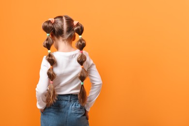 Little girl with beautiful hairstyle on orange background, back view. Space for text