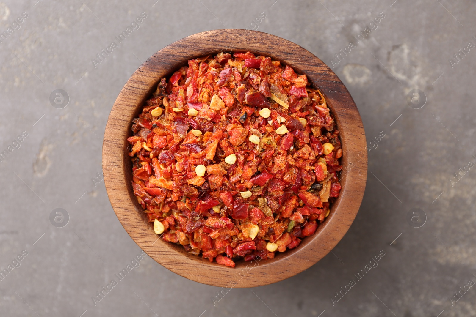 Photo of Chili pepper flakes in bowl on grey table, top view