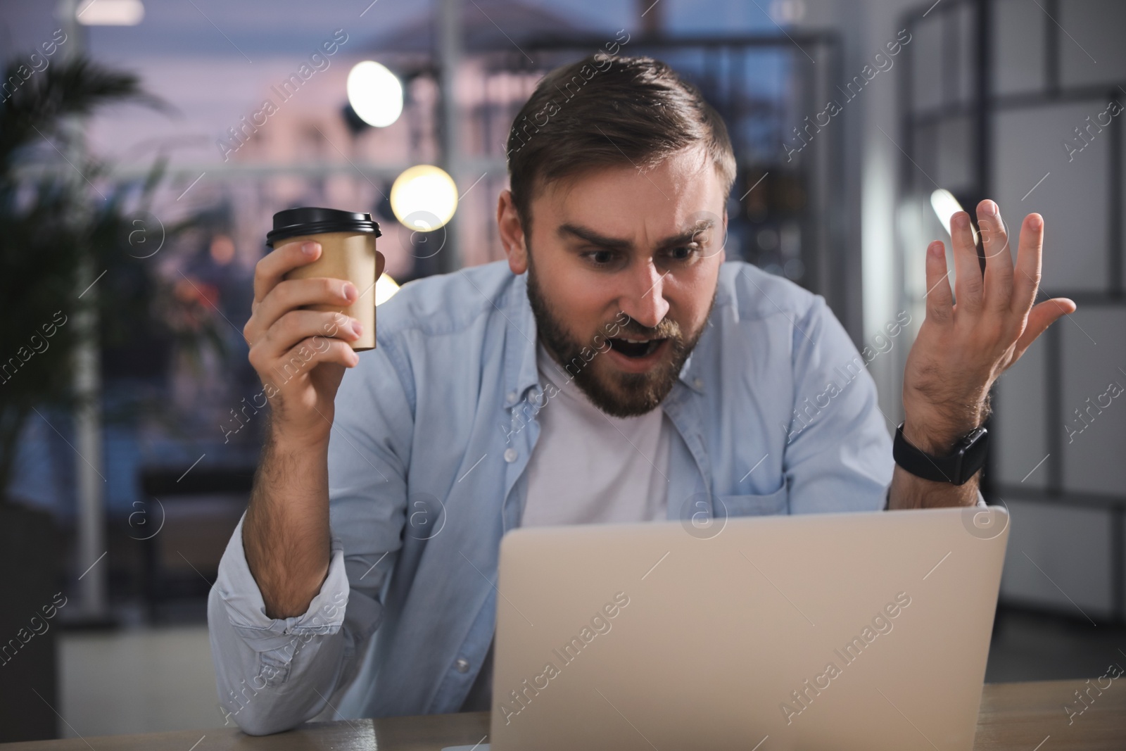 Photo of Emotional young man working on laptop in office. Online hate concept