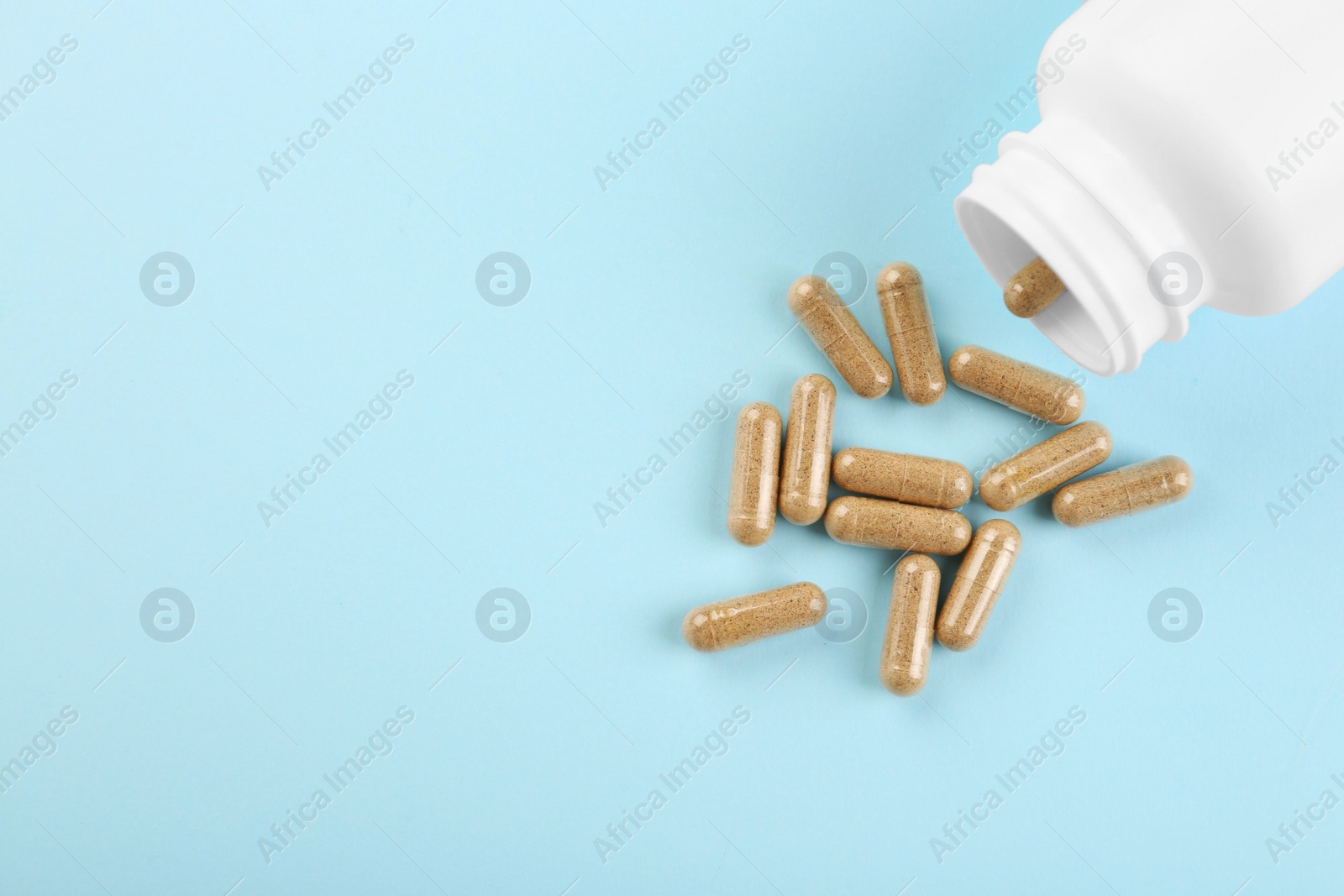 Photo of Bottle and vitamin capsules on light blue background, top view. Space for text