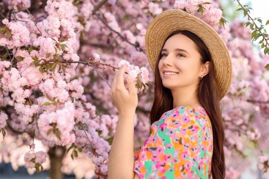 Beautiful woman in straw hat near blossoming tree on spring day