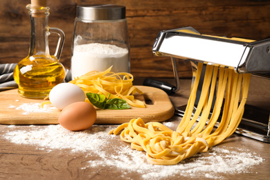 Photo of Pasta maker machine with dough and products on wooden table