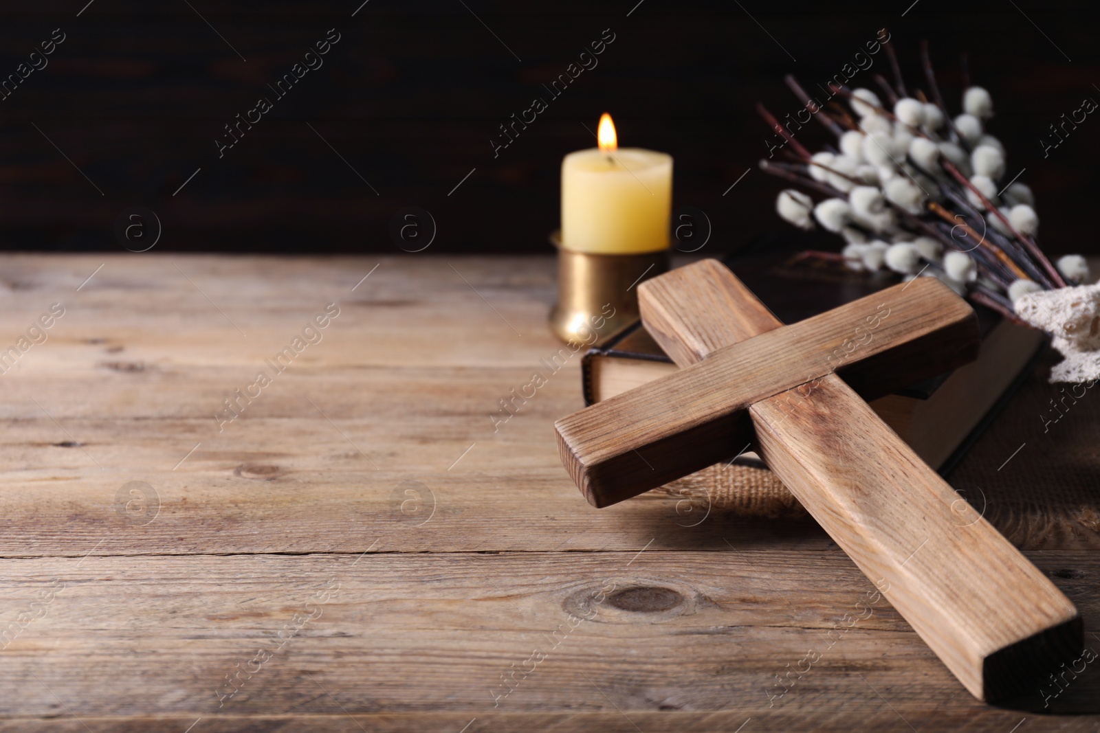 Photo of Burning church candle, cross, Bible and willow branches on wooden table. Space for text