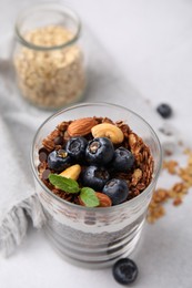 Photo of Tasty granola with berries, nuts, yogurt and chia seeds in glass on light table, closeup