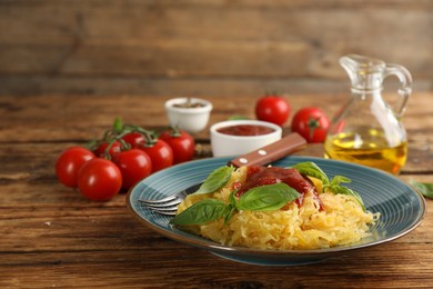 Photo of Tasty spaghetti squash with tomato sauce and basil served on wooden table