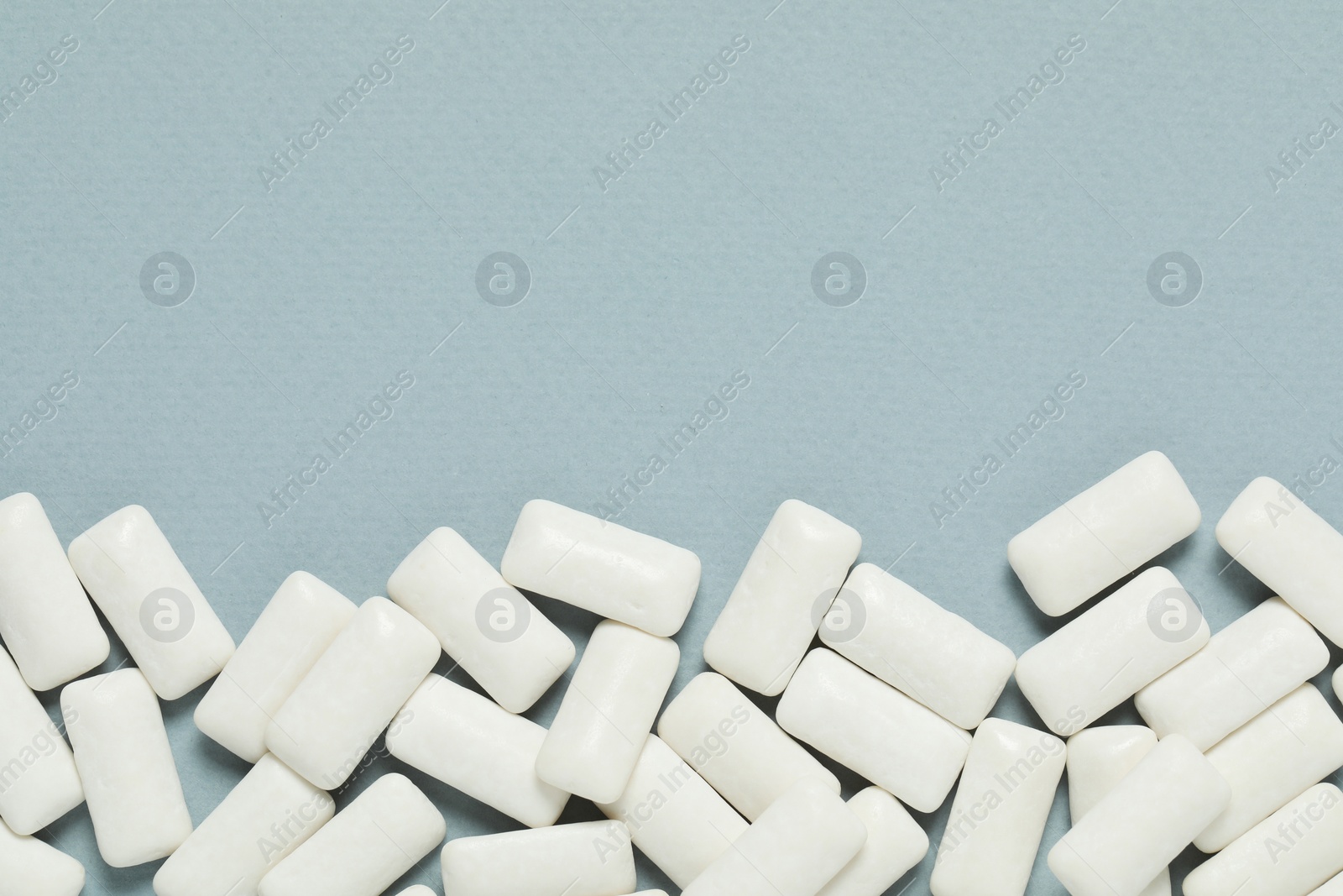 Photo of Tasty white chewing gums on light blue background, top view. Space for text