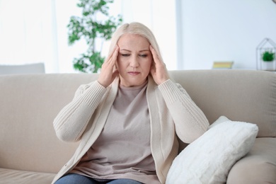 Mature woman suffering from headache while sitting on sofa at home