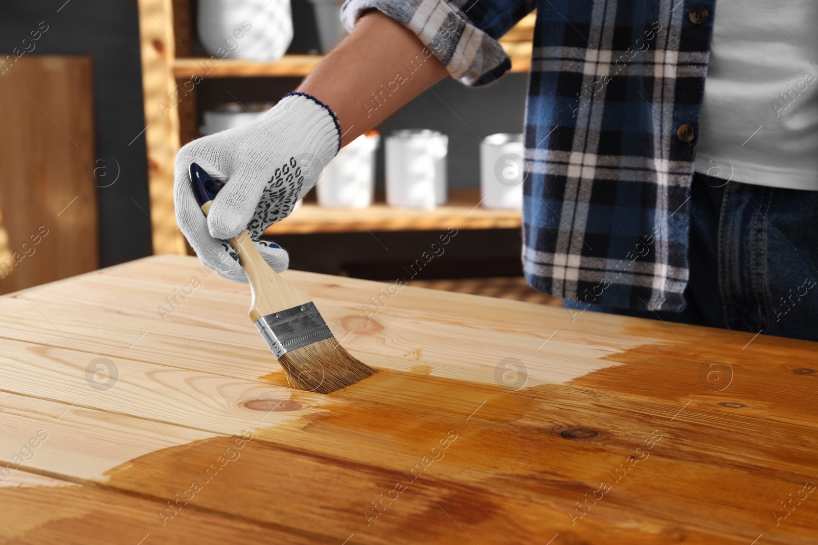 Photo of Man with brush applying wood stain onto wooden surface indoors, closeup