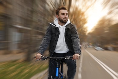 Image of Happy handsome man riding bicycle in city, motion blur effect