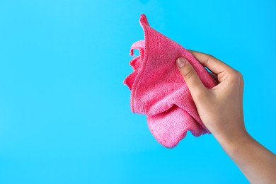 Photo of Woman holding microfiber cloth on light blue background, closeup. Space for text