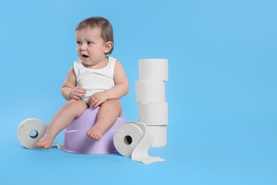 Little child sitting on baby potty and stack of toilet paper rolls against light blue background. Space for text