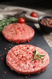 Photo of Raw hamburger patties with rosemary and peppercorns on slate plate, closeup