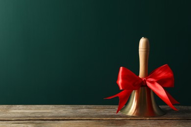 Golden bell with red bow on wooden table near green chalkboard, space for text. School days