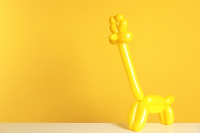 Photo of Giraffe figure made of modelling balloon on table against color background. Space for text