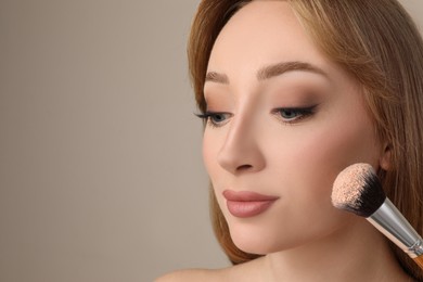 Beautiful young woman applying face powder with brush on grey background, closeup. Space for text