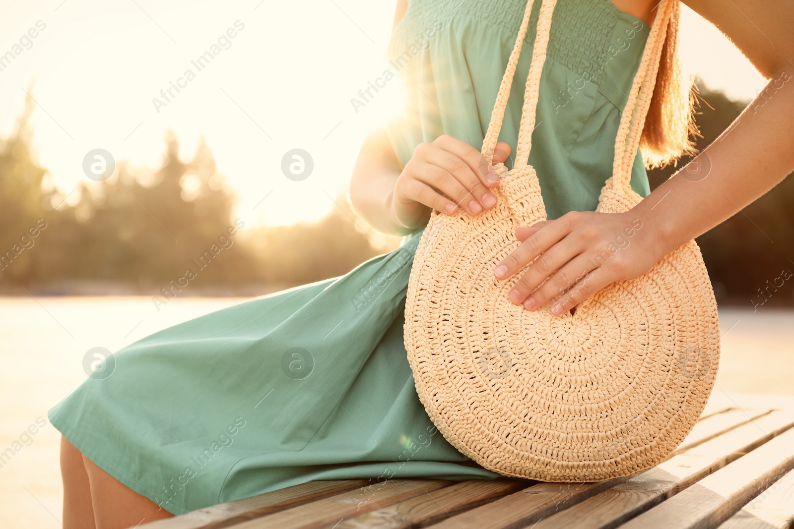 Photo of Young woman with stylish straw bag on bench outdoors, closeup