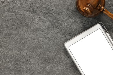 Modern tablet and gavel on gray textured table, flat lay. Space for text