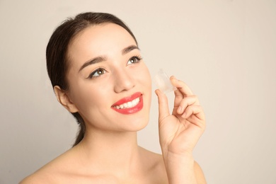 Young woman with ice cube on light background. Skin care