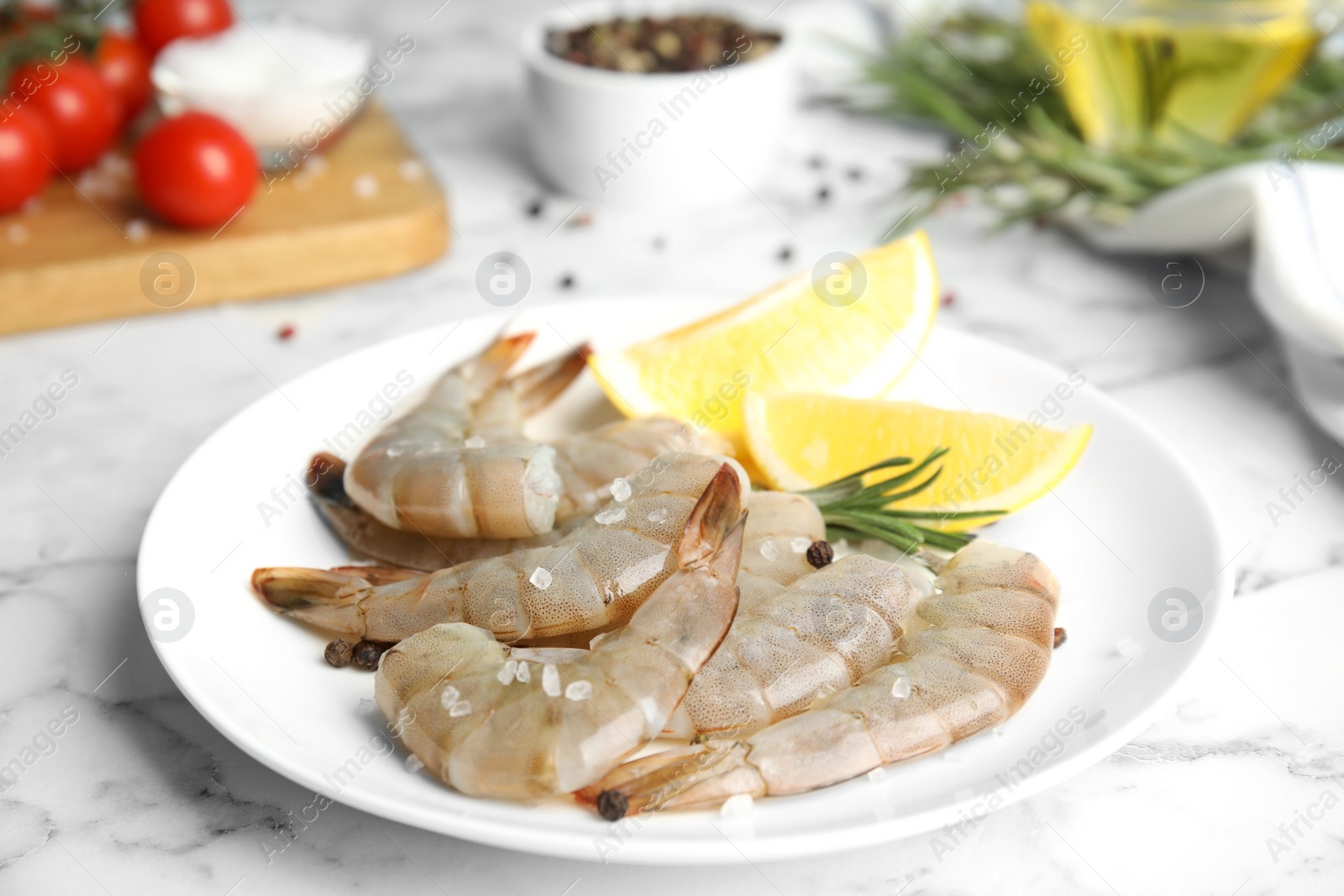 Photo of Fresh raw shrimps with lemon and rosemary on marble table