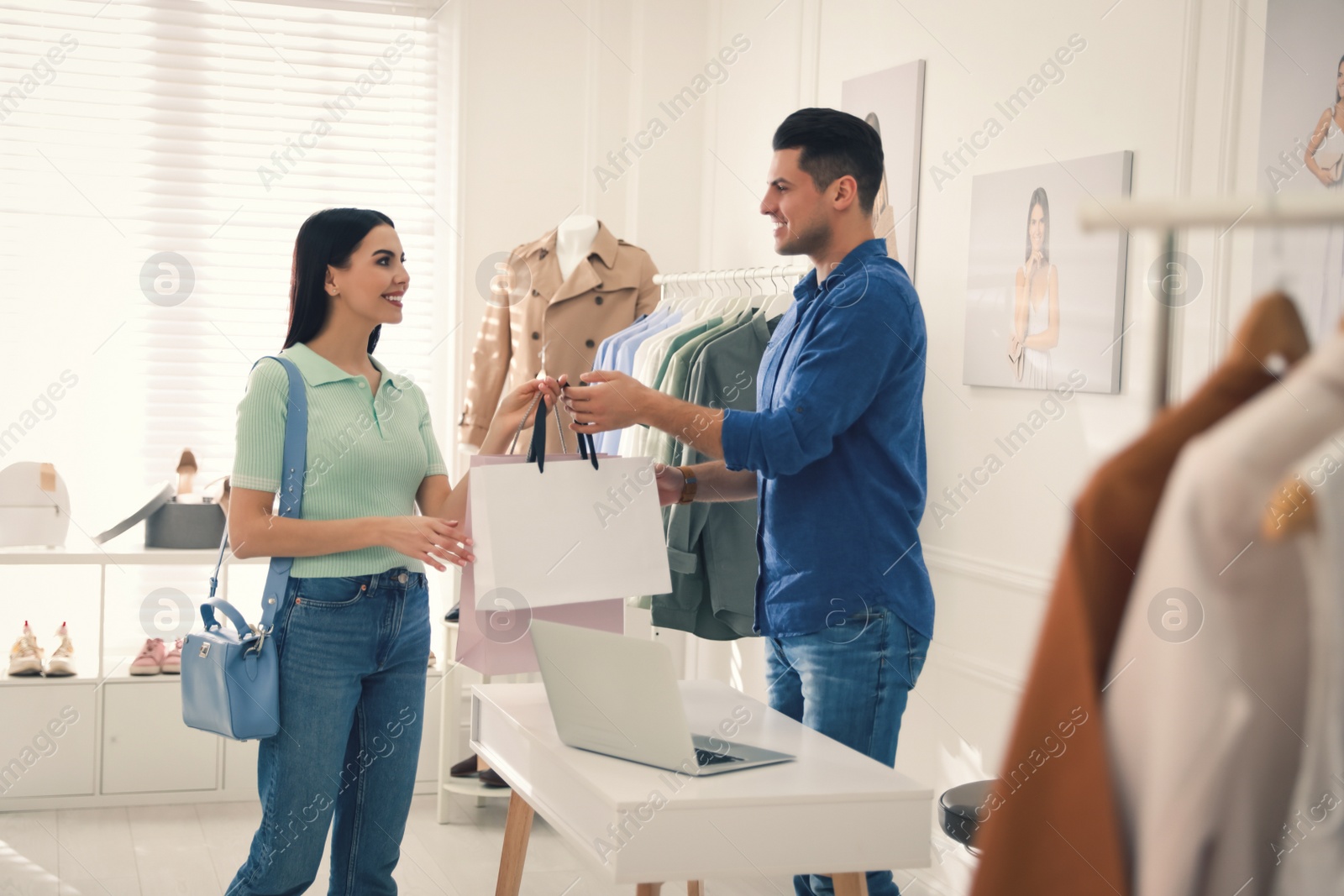 Photo of Shop assistant giving bags with clothes to customer in modern boutique