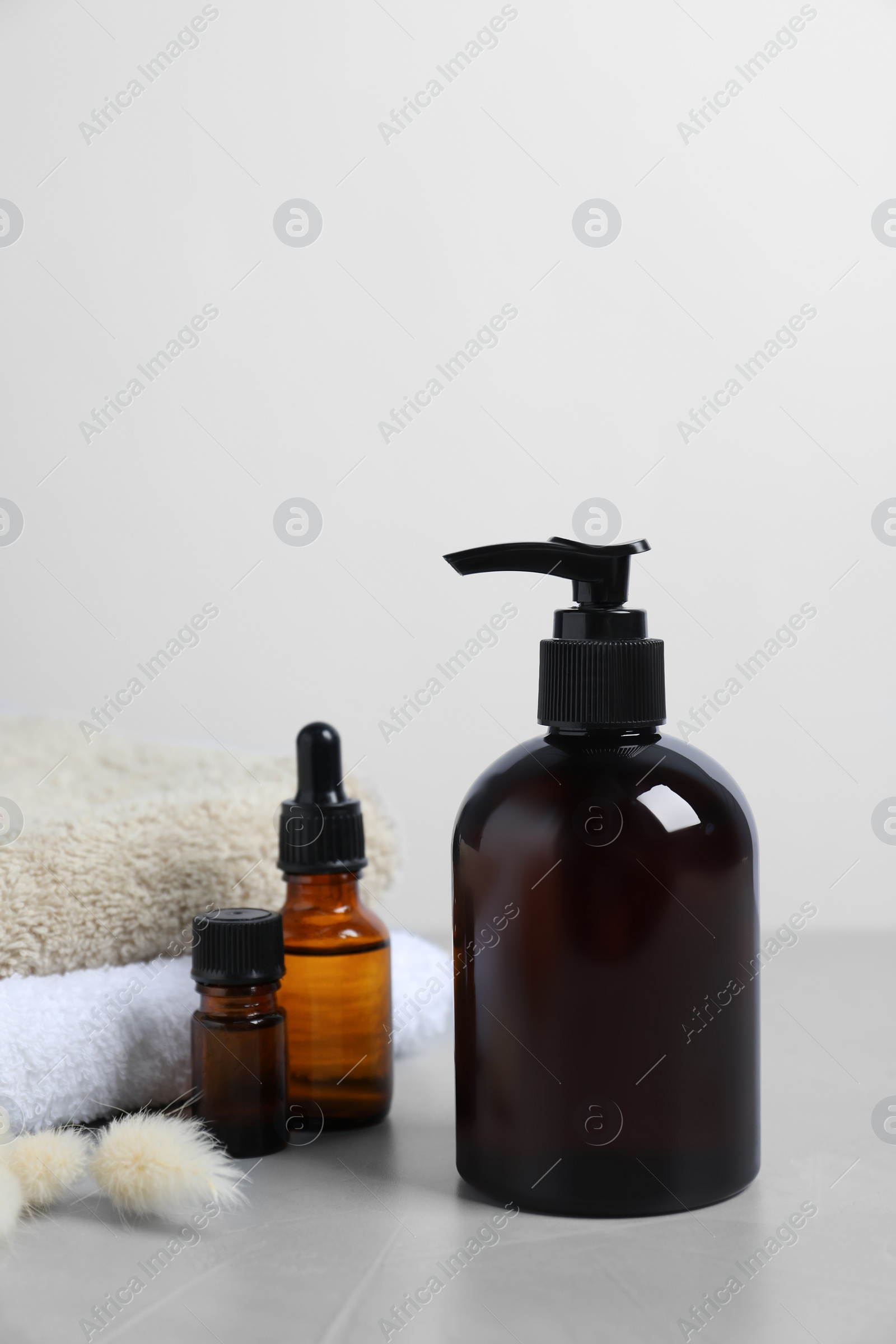 Photo of Bottles with different cosmetic products, dry decorative spikes and soft towels on light grey table