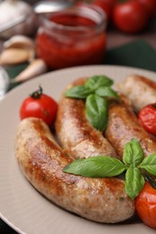 Photo of Plate with tasty homemade sausages, basil leaves and tomatoes, closeup