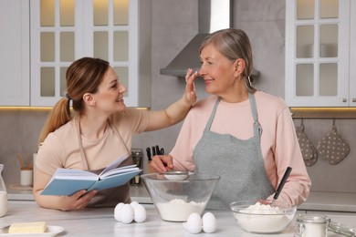 Happy women cooking by recipe book in kitchen