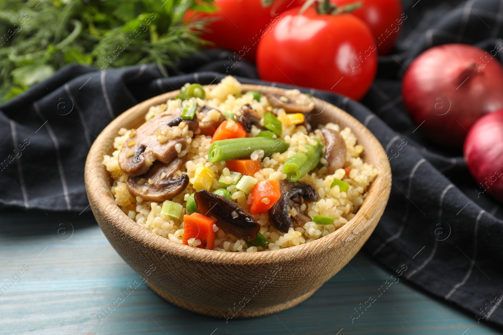 Photo of Delicious bulgur with vegetables and mushrooms on light blue wooden table, closeup