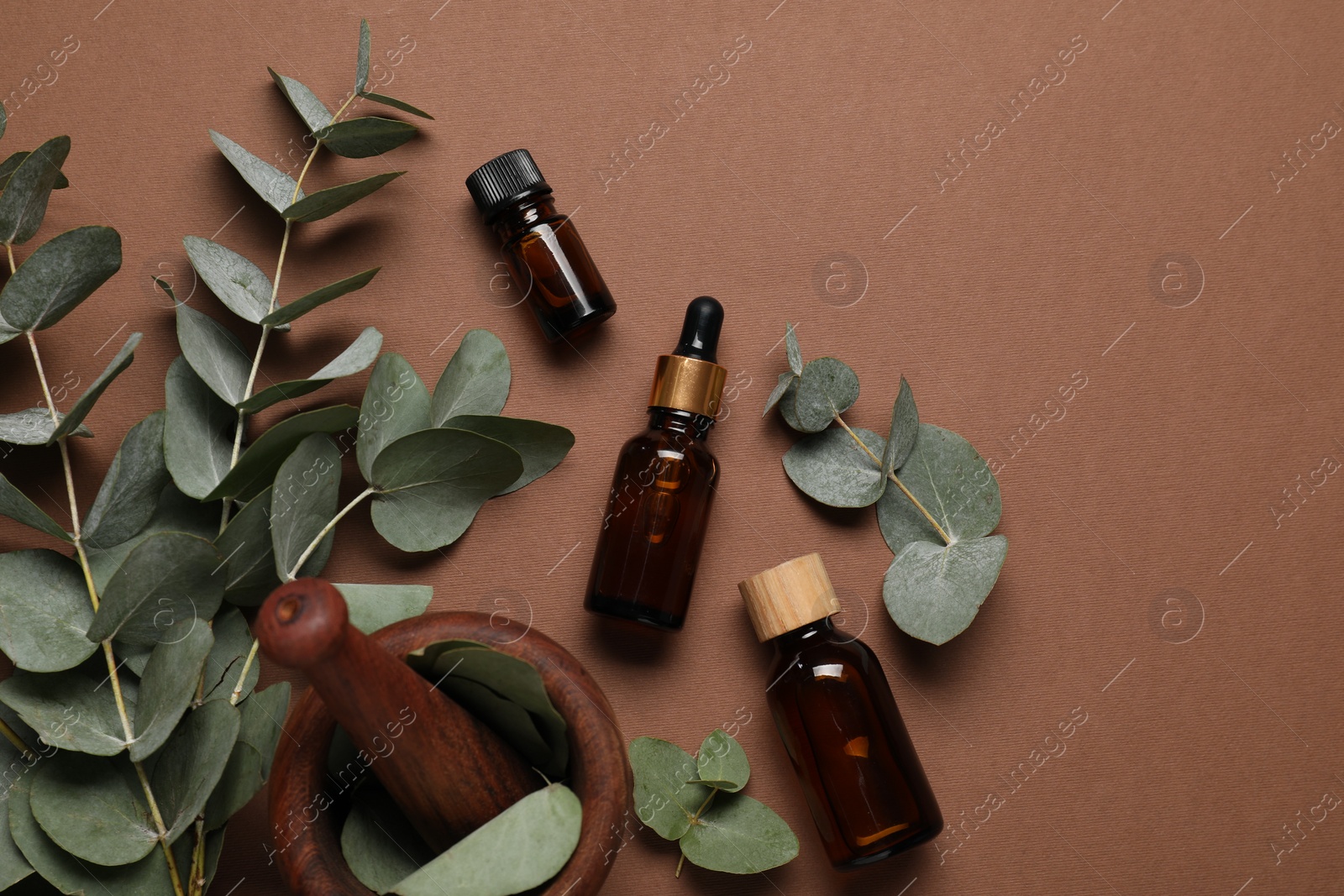 Photo of Aromatherapy. Bottles of essential oil, mortar and eucalyptus branches on brown background, flat lay