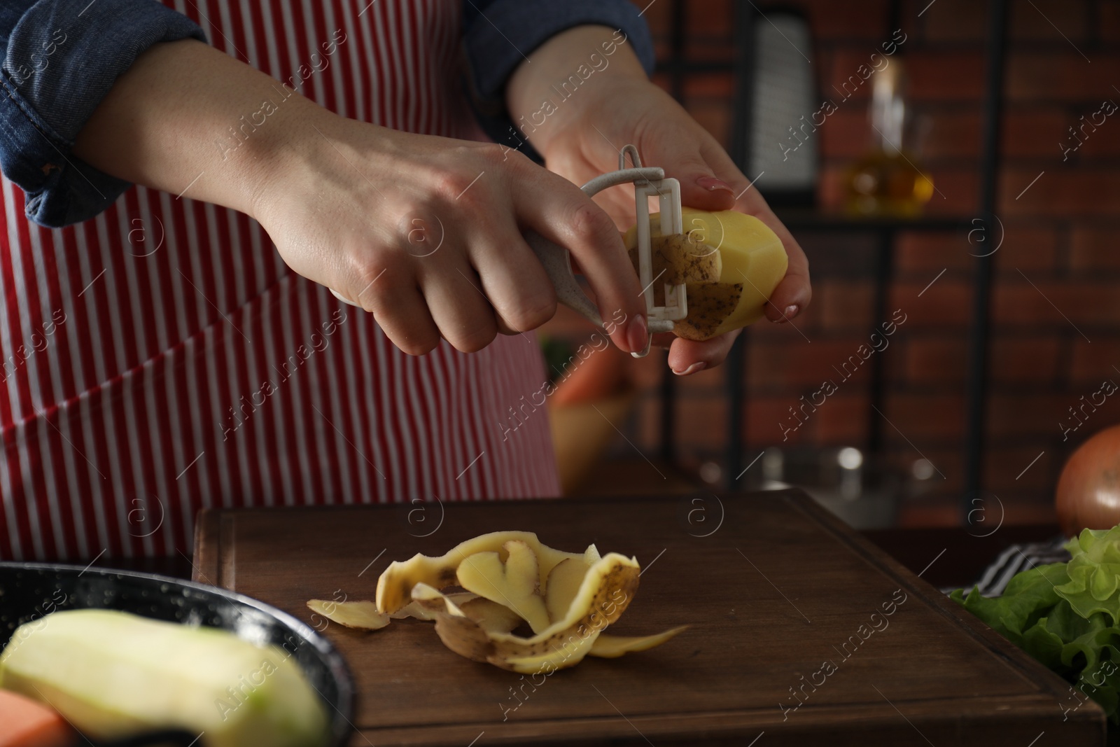 Photo of Woman peeling fresh potato at table indoors, closeup