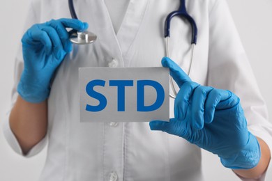 Photo of Doctor holding sheet of paper with abbreviation STD on white background, closeup