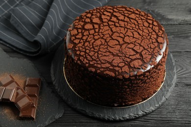Photo of Delicious truffle cake and chocolate pieces on black wooden table