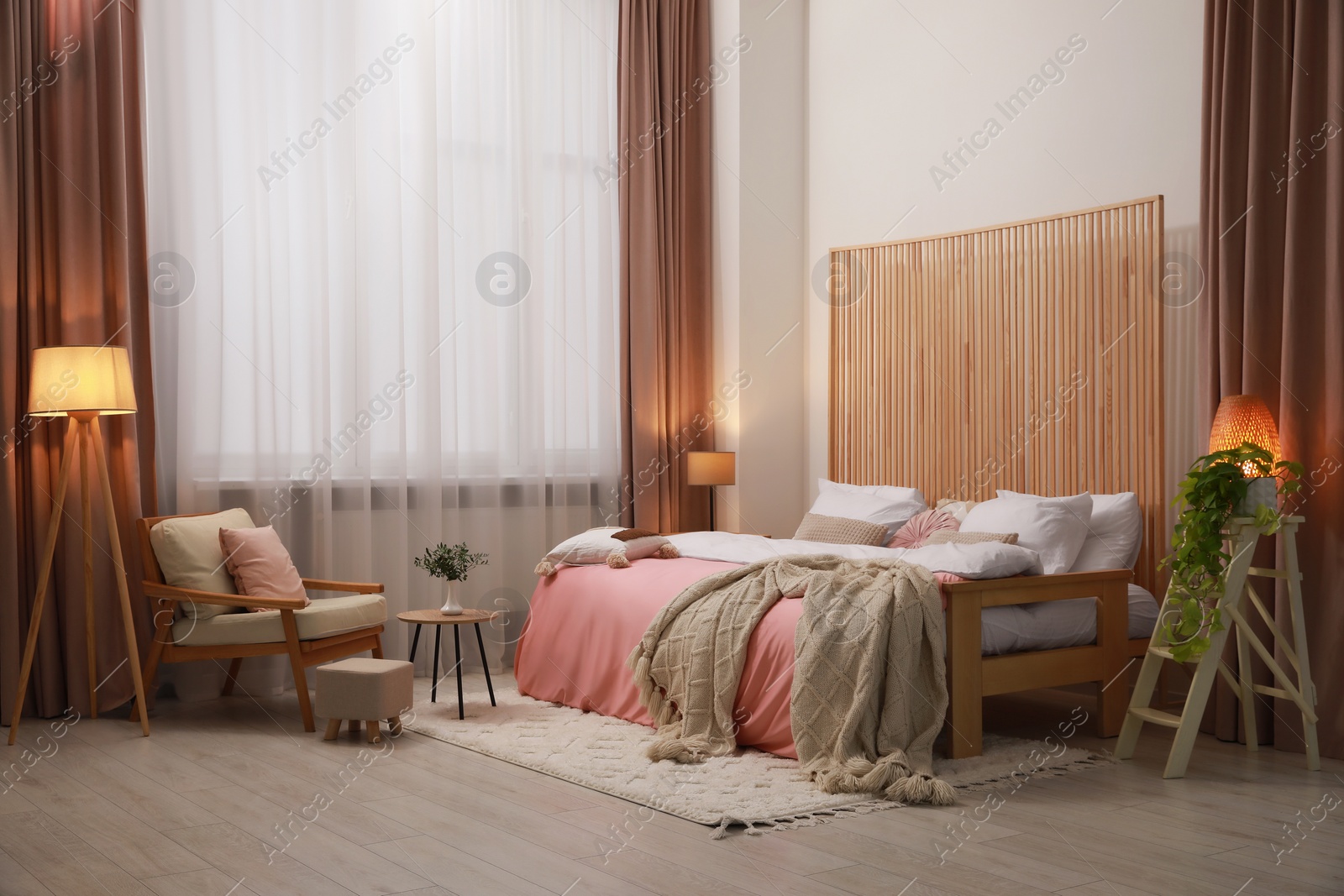 Photo of Stylish bedroom with comfortable bed, armchair and wooden table. Interior design
