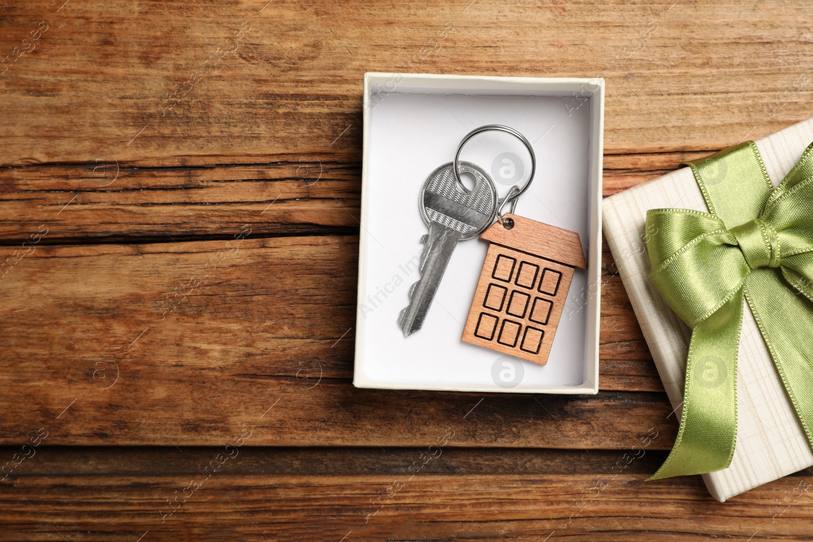 Photo of Key with bow in gift box on wooden table, flat lay and space for text. Housewarming party