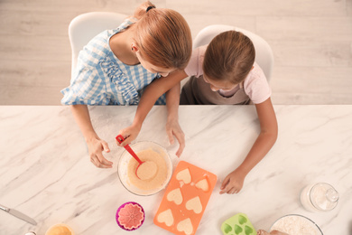 Mother and daughter making cupcakes together in kitchen, top view