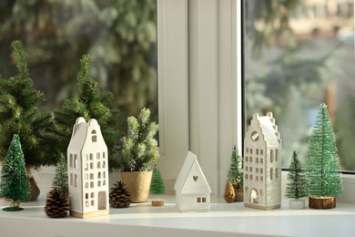 Photo of Beautiful house shaped candle holders and small fir trees on windowsill indoors