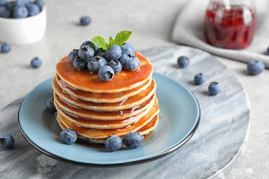 Photo of Plate of delicious pancakes with fresh blueberries and syrup on grey table