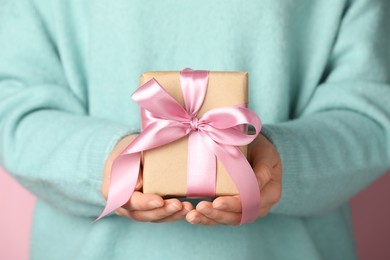 Woman holding gift box with bow on pink background, closeup